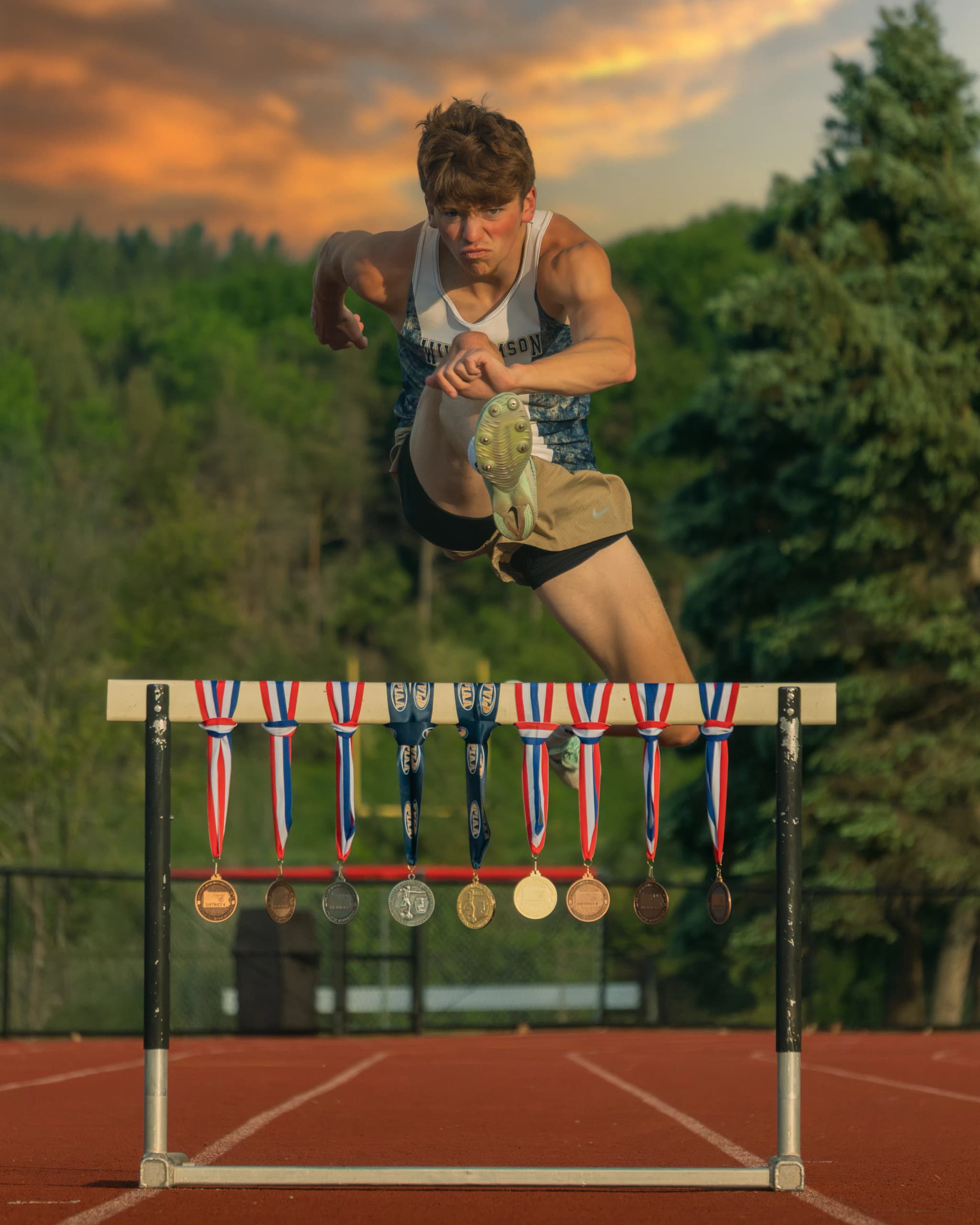 Duncan Kerr clearing a hurdle hung with his medals, a sunset sky behind him