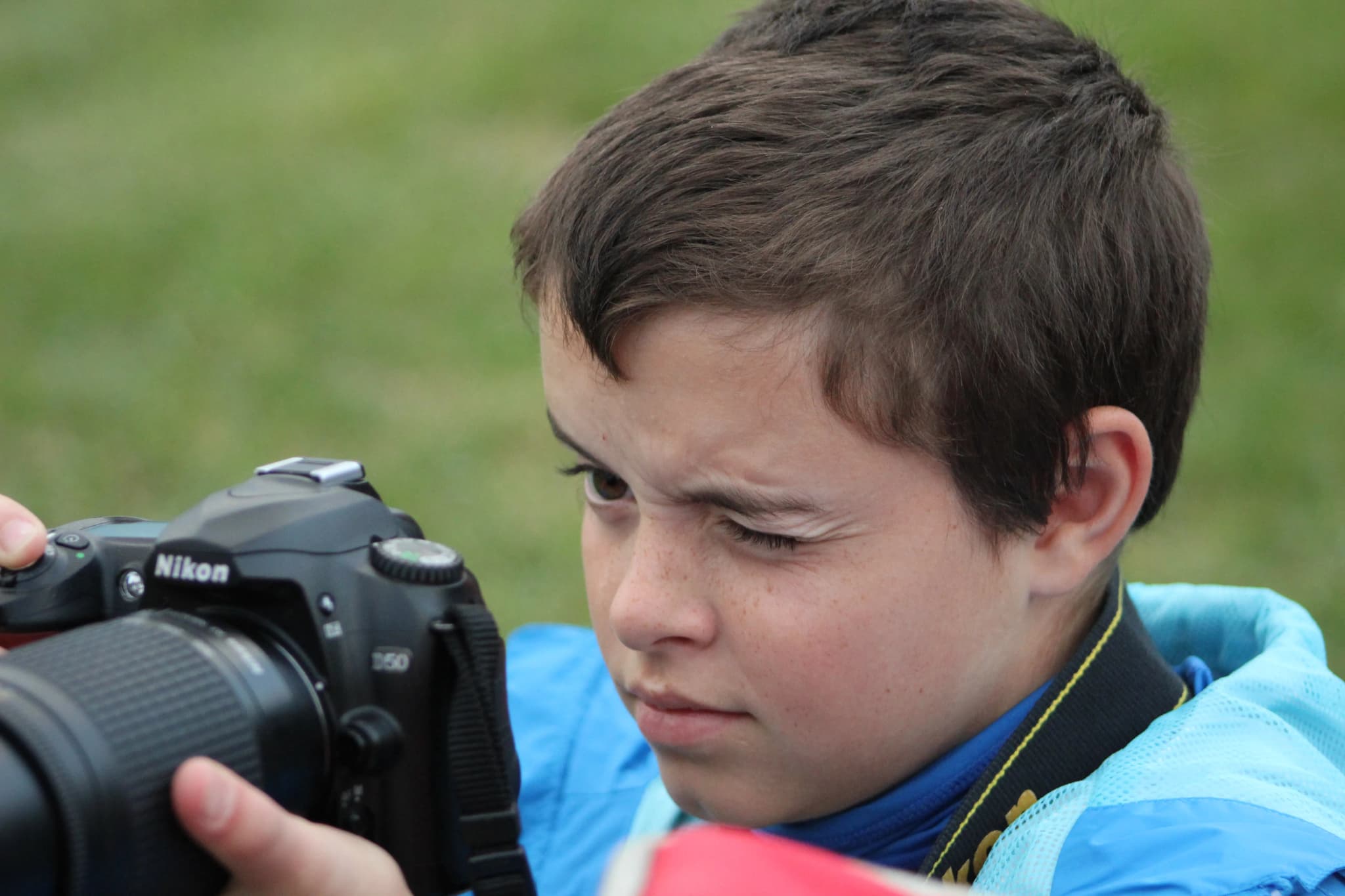 Cole as a kid, squinting while holding a DSLR on a grass field