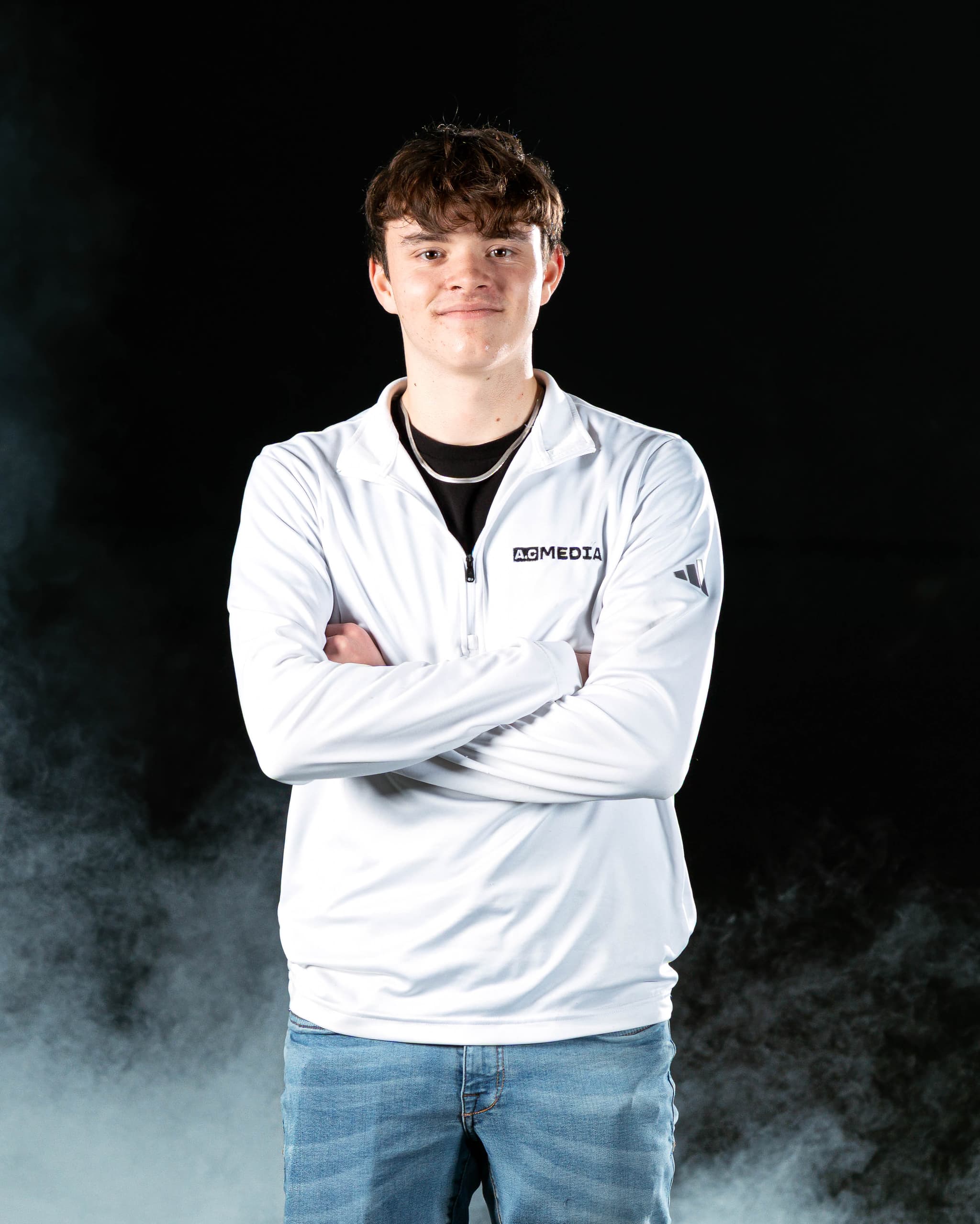 Cole with arms crossed in an A.C Media quarter zip, smoke drifting across a black backdrop